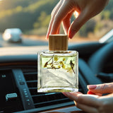 Person holding a clear perfume bottle with a wooden cap inside a car.