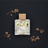 Clear perfume bottle with wooden cap on a dark background with dried flowers