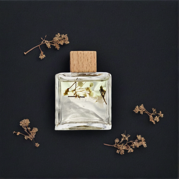 Clear perfume bottle with wooden cap on a dark background with dried flowers
