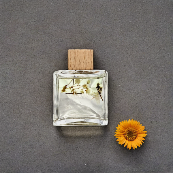 Clear glass perfume bottle with wooden cap and pressed flowers on a gray background, accompanied by a sunflower.
